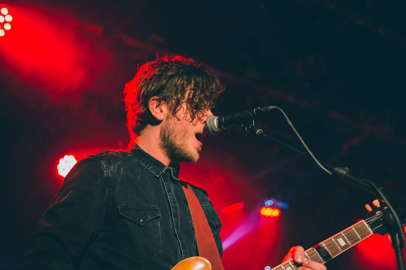 Singer performing with a guitar under red stage lights
